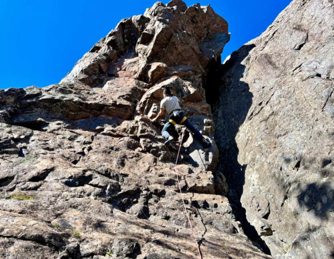 A person climbs a steep rock face with a line of rope stretching from the ground up to their harness. 